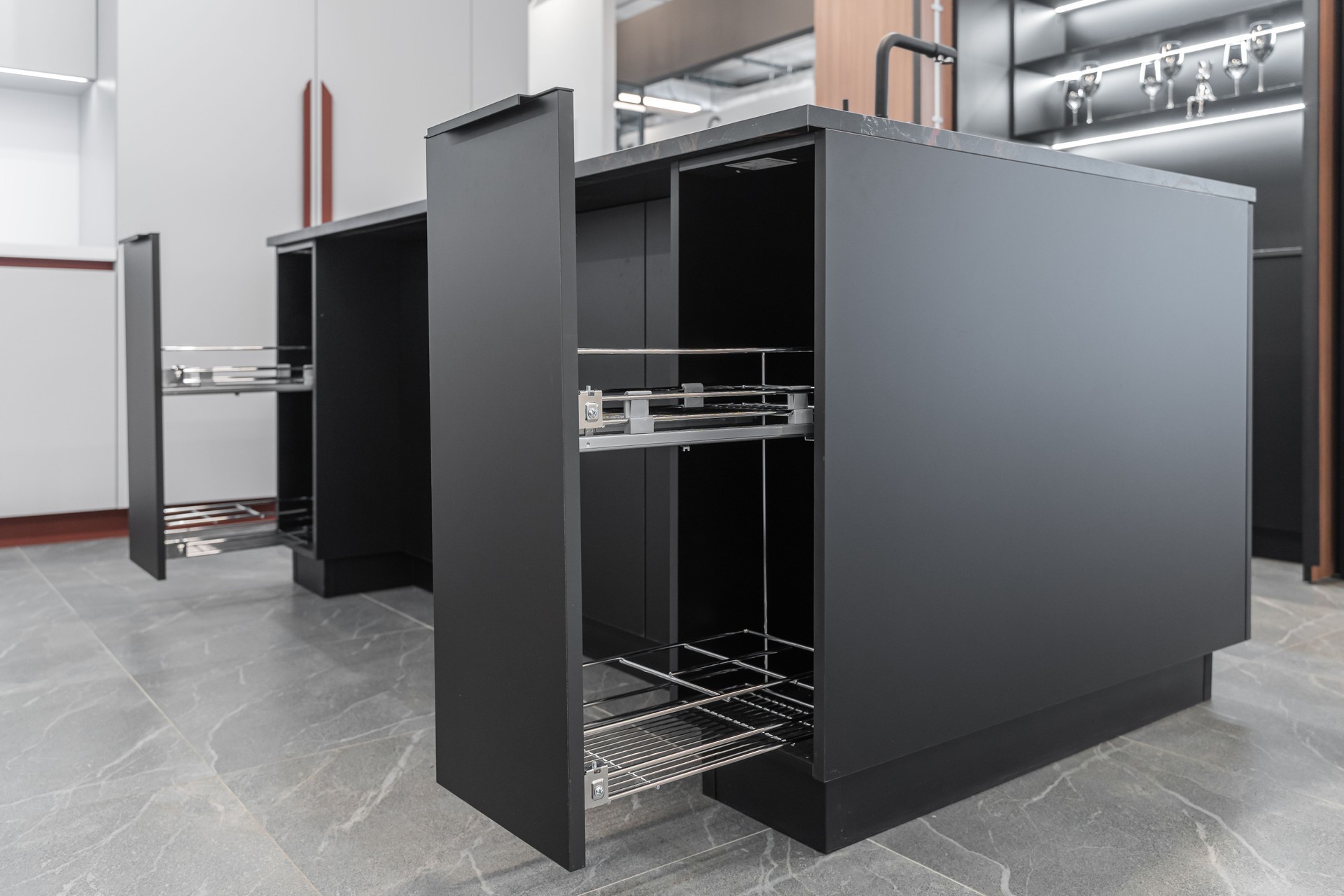 modern built-in kitchen. kitchen island with black marble countertop. drawers are open and reveal shelves for storage. Kitchen with wooden doors. glasses and kitchen utensils on the shelves.
